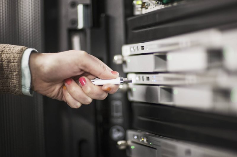 Computer techniican inserting thumb drive into a server in a server farm. Computer techniican inserting thumb drive into a server in a server farm.